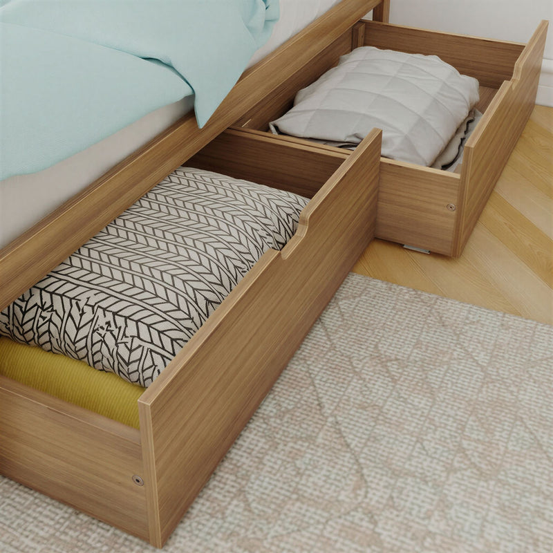Wooden underbed storage drawers open beneath a bed with folded blankets and pillows — space-saving bedroom storage solution