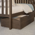 Close-up of dark brown wooden bunk bed with pull-out trundle storage drawer, white linen mattress and light blue throw, modern bedroom furniture