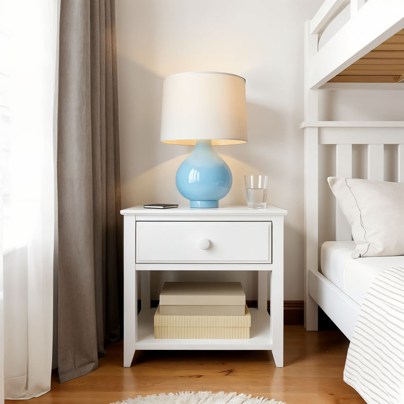 White bedside table with blue ceramic lamp, glass of water, smartphone, and books in a cozy modern bedroom.