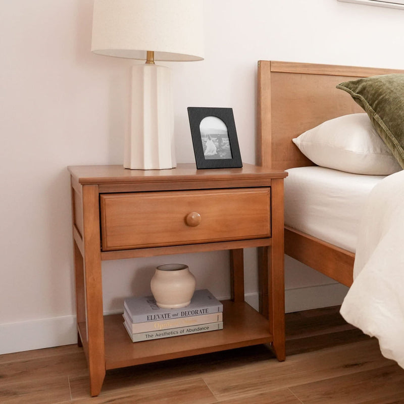 Wooden bedside table with a lamp and framed photo beside a bed in a modern bedroom.