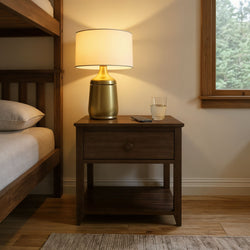 Wooden nightstand with a modern gold lamp, smartphone, and glass of water in a cozy bedroom.