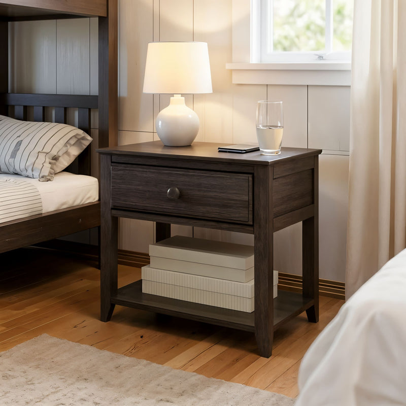 Wooden bedside table in a cozy bedroom setting, featuring a lamp, glass of water, and books, with natural light from the window.