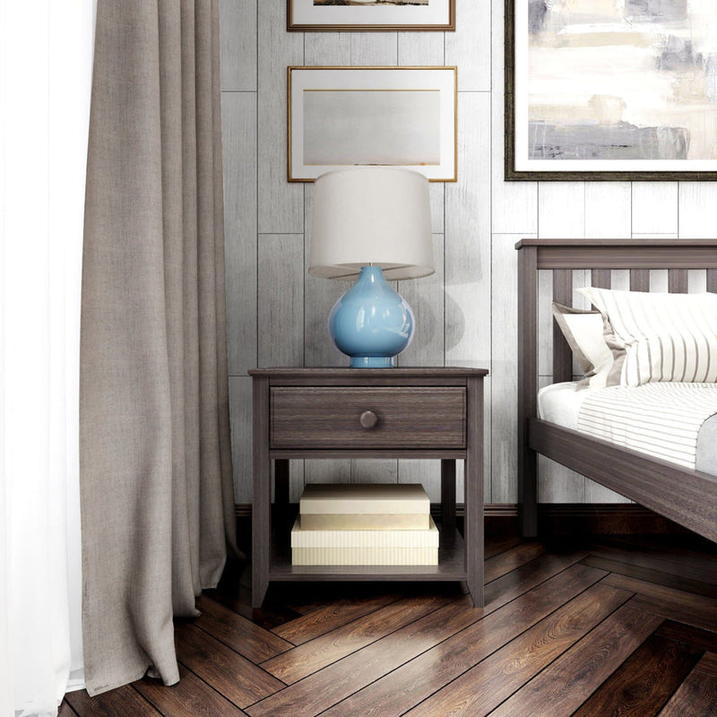 Wooden bedside table with a drawer and a blue lamp, next to a bed in a modern bedroom setting.