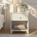 White nightstand with ceramic table lamp and glass vase holding pilea (Chinese money plant) on wooden floor in minimalist neutral bedroom decor