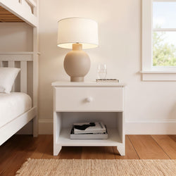 Modern bedroom with white nightstand, beige lamp, and books, showcasing minimalist decor.