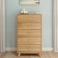 Mid-century modern natural pine five-drawer tall dresser with round knobs in a minimalist bedroom with light blue wall, decorative candles and beach wall art