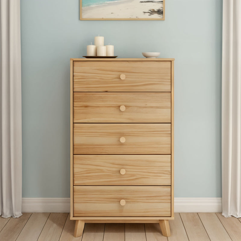 Mid-century modern natural pine five-drawer tall dresser with round knobs in a minimalist bedroom with light blue wall, decorative candles and beach wall art