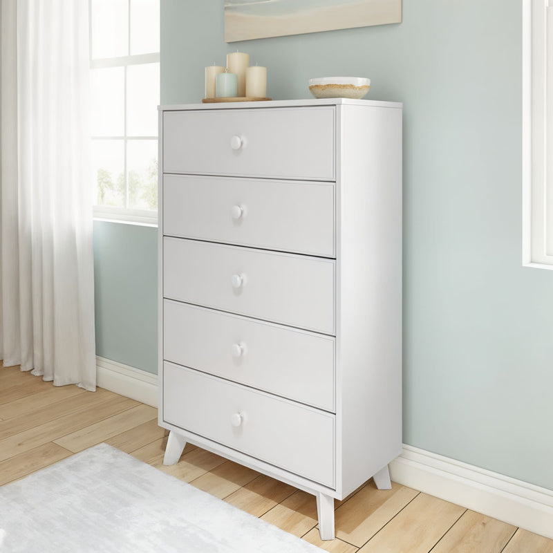 Modern white tall five-drawer dresser with angled mid-century legs in a bright bedroom with pastel blue wall, hardwood floor, window light and decorative candles