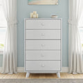 Modern white 5-drawer wooden dresser against a light blue wall with candles and a bowl on top, flanked by white curtains in a coastal-style bedroom
