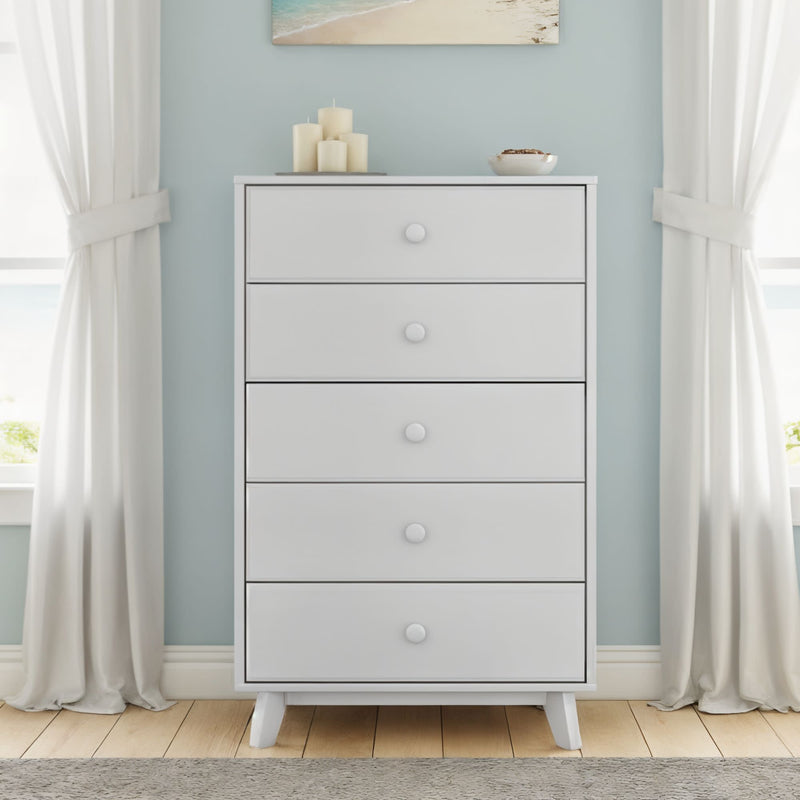 Modern white 5-drawer wooden dresser against a light blue wall with candles and a bowl on top, flanked by white curtains in a coastal-style bedroom