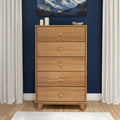 Oak five-drawer tall dresser on hardwood floor against navy blue accent wall with white curtains, minimalist decor and candles, modern bedroom storage