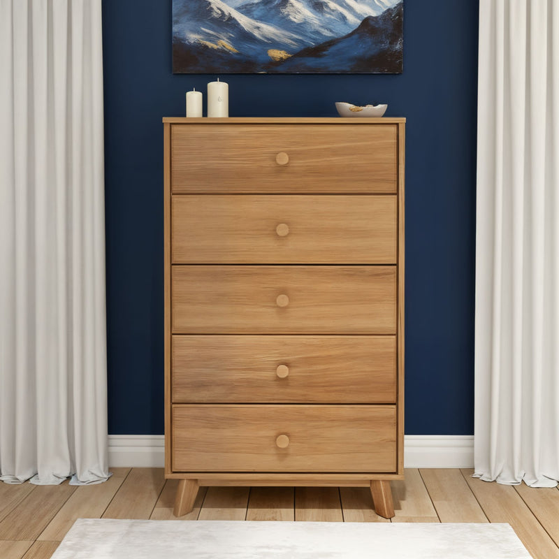 Oak five-drawer tall dresser on hardwood floor against navy blue accent wall with white curtains, minimalist decor and candles, modern bedroom storage
