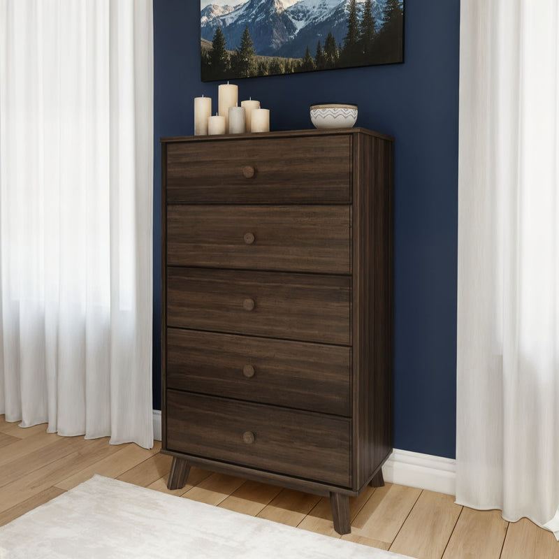 Mid-century modern dark wood five-drawer dresser with tapered legs in a bedroom with navy accent wall, white curtains, and hardwood floor.