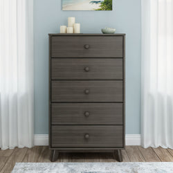 Gray five-drawer wooden dresser (tall chest of drawers) in light-blue bedroom with white curtains, hardwood floor, and decorative candles and bowl on top — mid-century modern storage furniture