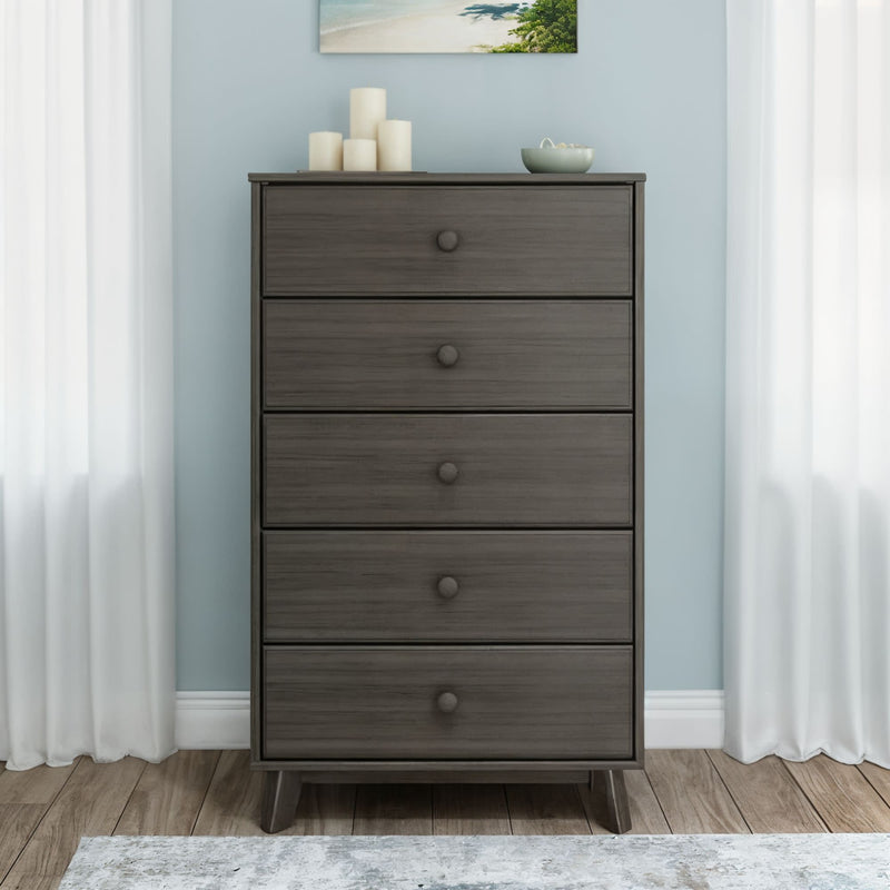 Gray five-drawer wooden dresser (tall chest of drawers) in light-blue bedroom with white curtains, hardwood floor, and decorative candles and bowl on top — mid-century modern storage furniture