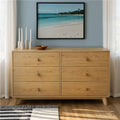 Oak six-drawer dresser with round knobs in a minimalist mid-century modern bedroom, beach wall art, candles and hardwood floor
