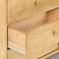 Open wooden dresser drawer in light pine finish showing wood grain, wooden knob, and metal side rail — bedroom storage furniture