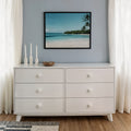 White six-drawer dresser with round knobs in minimal coastal bedroom decor, framed beach wall art, three white candles, wooden bowl, sheer curtains, hardwood floor