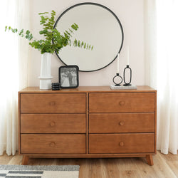 Wooden dresser with round mirror, decorative plants, and candles in minimalist modern bedroom.