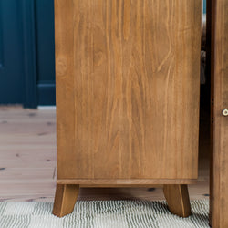 Mid-century modern wooden cabinet with natural grain details on a striped rug in a home interior setting.