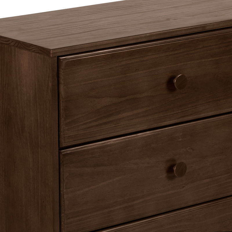 Close-up of a dark brown solid wood dresser with three drawers and round knob handles, smooth wood-grain finish on a modern bedroom chest of drawers