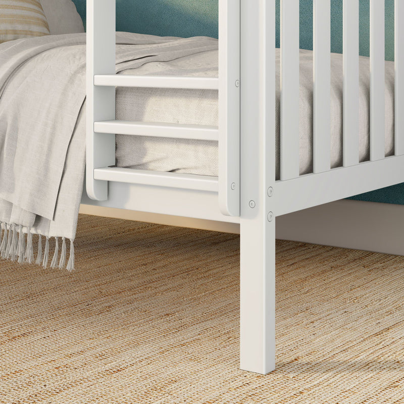 Close-up of white wooden bed rail with beige linen blanket and natural jute rug – modern nursery decor
