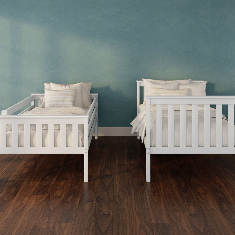 Two white wooden twin beds with neutral striped pillows in a modern nursery against a teal textured wall and dark hardwood floor