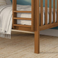 Close-up of a solid wood slatted bed frame with neutral linen bedding, fringed throw blanket, and woven jute rug against a teal accent wall