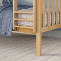 Close-up of light wood bunk bed ladder and slatted frame with blue quilted bedding and ribbed white mattress over a textured woven area rug