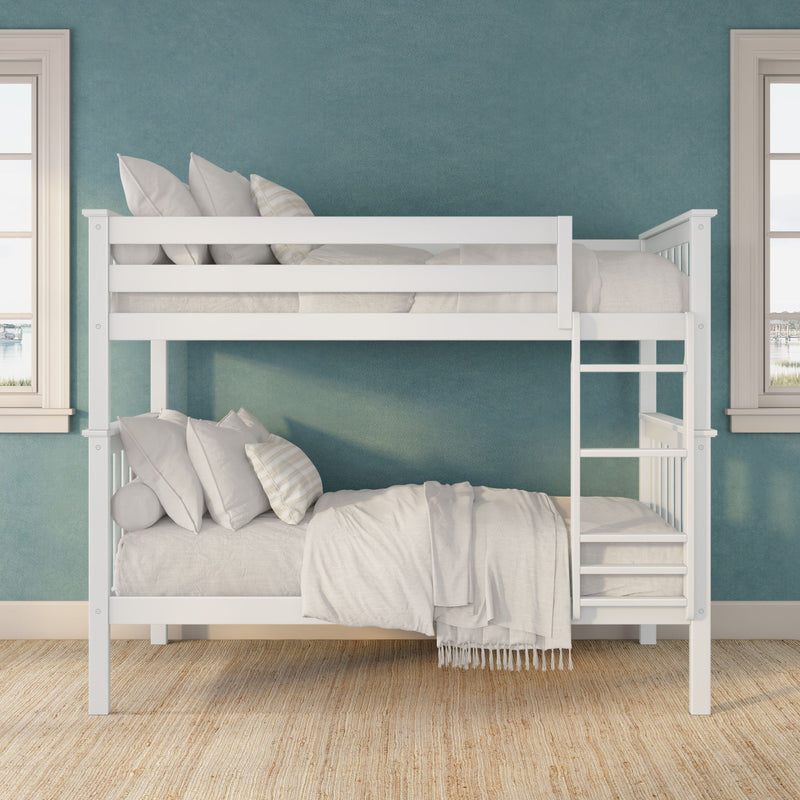 White wooden bunk bed with ladder, white linens and pillows against teal accent wall in bright kids’ bedroom with natural woven rug and twin windows