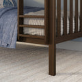 Close-up of dark walnut wooden bed frame slats and corner with blue quilted blanket, cream ribbed mattress cover and woven gray area rug