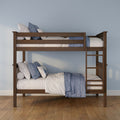 Solid wood twin-over-twin bunk bed with ladder, blue-and-white quilted bedding and pillows against a light blue wall on hardwood floors