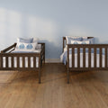 Wooden twin beds with blue and white bedding against a light blue wall on warm hardwood floors – coastal-style children's bedroom decor
