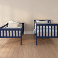 Two navy blue twin beds with white and blue floral pillows on hardwood floor against a neutral beige wall in a modern kids' bedroom nursery