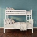 White wooden twin-over-twin bunk bed with ladder, beige linens and pillows against a teal textured wall over dark hardwood floor