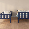 Two navy blue twin beds with floral pillows and light blue bedding against a neutral beige wall on hardwood floor