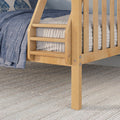 Close-up of light maple wooden bunk bed ladder and slats with blue quilted bedding and textured woven rug