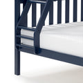Close-up of navy blue wooden bunk bed ladder and side rail with white quilted mattress, modern sturdy kids bed frame