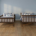 Two wooden twin beds with blue and white bedding against a pale blue wall and hardwood floor, coastal twin bedroom decor