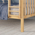 Close-up of light wood bunk bed ladder and slatted guardrail with blue quilted bedding and gray textured rug