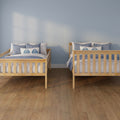 Two twin wooden beds with blue and white bedding and coastal pillows against a light blue wall on hardwood flooring