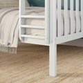 Close-up of white wooden crib corner with beige linen bedding and textured woven jute rug, modern nursery decor.