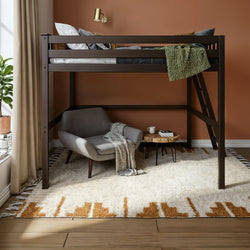Dark wood loft bed with ladder over cozy reading nook featuring gray armchair, wooden side table, textured cream-and-tan rug and terracotta accent wall
