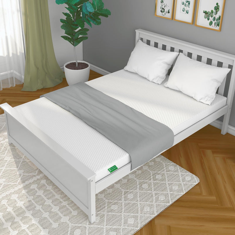 White wooden bed frame with white mattress and pillows, gray blanket, green plant, geometric rug, and framed wall art in a modern bedroom.