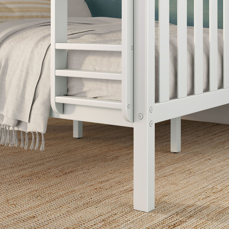 Close-up of white slatted wooden bed frame and ladder with beige textured linen blanket and woven jute rug in a modern nursery bedroom