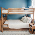 Solid wood twin-over-full bunk bed against a blue accent wall with white quilted bedding, neutral throw pillows and a wooden nightstand