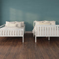 Two white wooden twin beds with beige linens and striped pillows against a teal textured accent wall on dark hardwood floor
