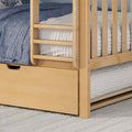 Close-up of a maple wooden bunk bed ladder and guardrail with blue and light‑gray textured quilts and an under‑bed storage drawer on a woven rug