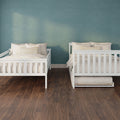 Two white wooden twin beds with neutral beige bedding and striped pillows against a teal textured accent wall over dark hardwood flooring — modern minimalist kids' bedroom
