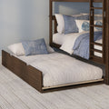 Wooden bunk bed with pull-out trundle, white quilted bedding and blue decorative pillows on a textured rug